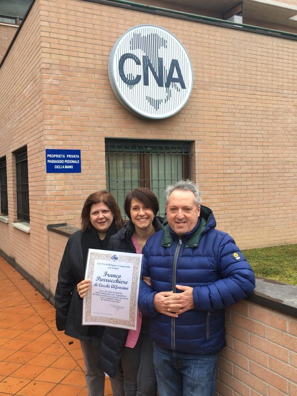 Maria Di Nuovo e Federica Scagliarini di Cna Bologna con Cocchi Alfonsino della ditta Franco Parrucchiere con la pergamena "Buon Anniversario" per i 35 anni di attività dell'azienda